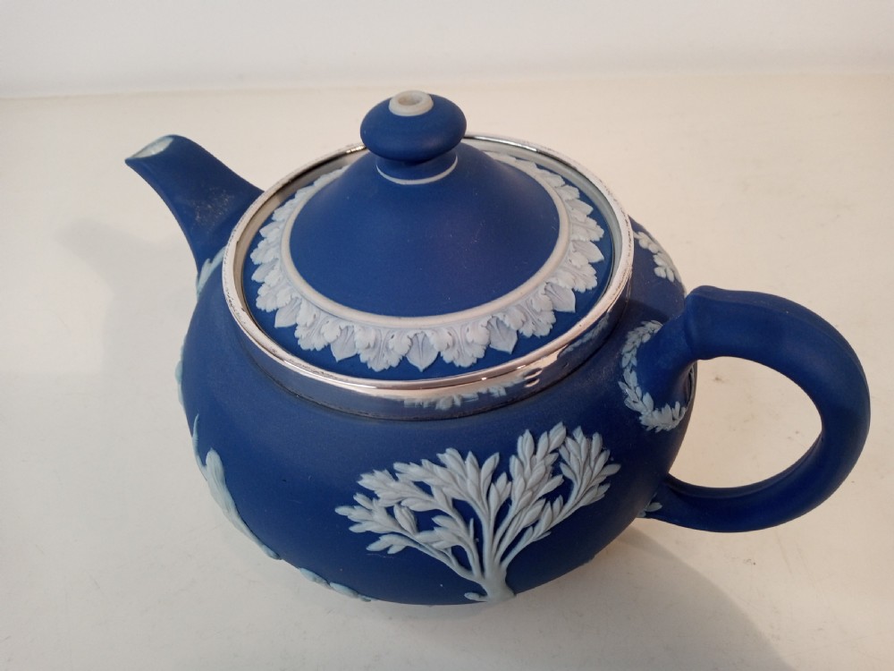 A blue stoneware teapot featuring white neoclassical bas-relief figures and a silver collar around the rim. View IV