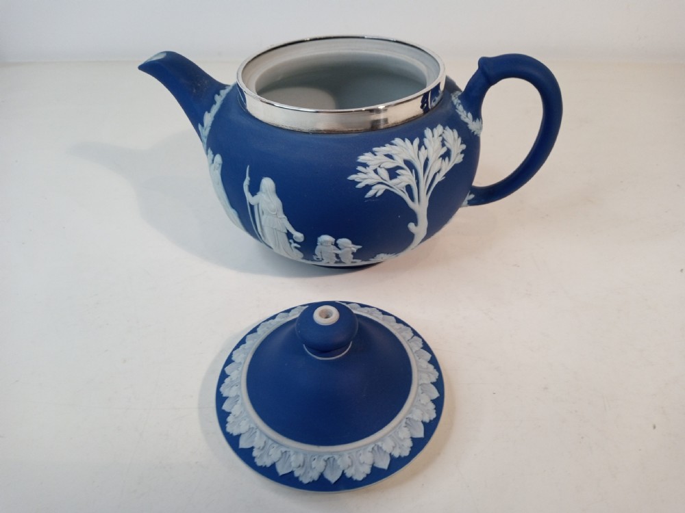 A blue stoneware teapot featuring white neoclassical bas-relief figures and a silver collar around the rim. View V