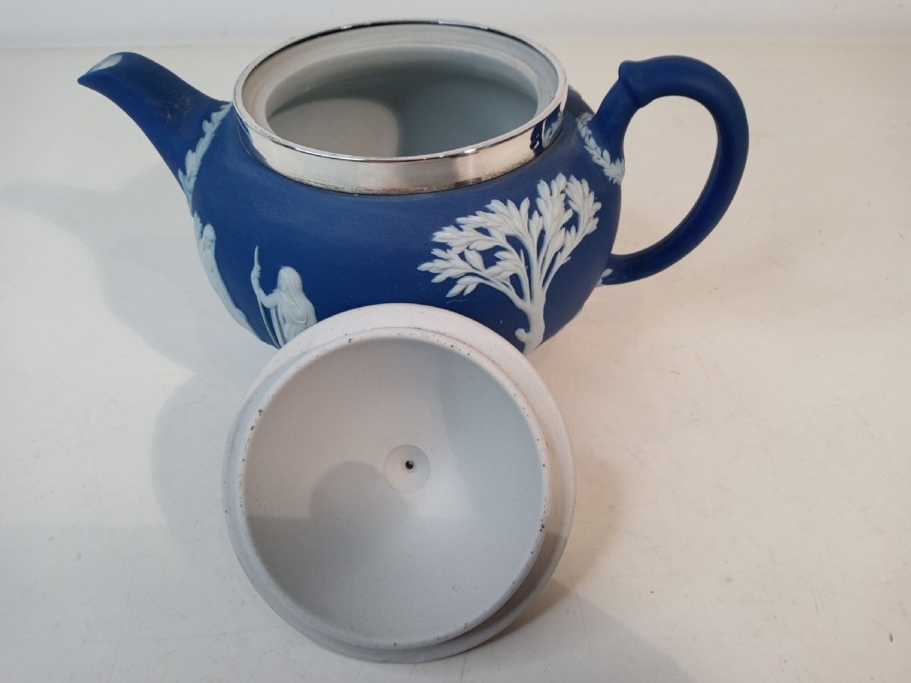 A blue stoneware teapot featuring white neoclassical bas-relief figures and a silver collar around the rim. View VI