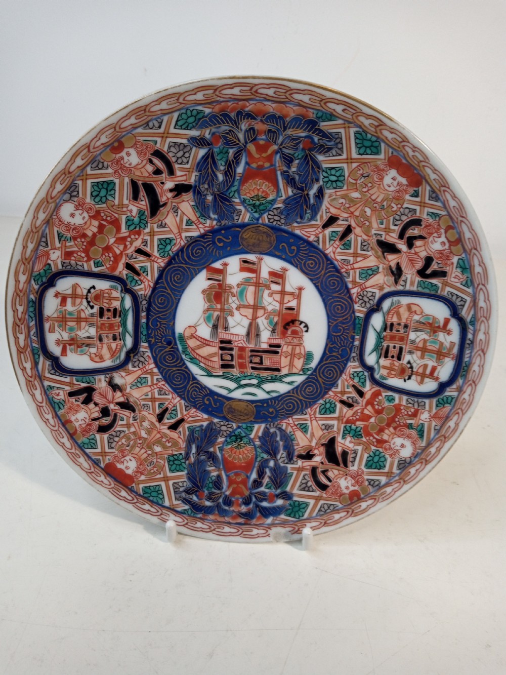 A four-piece Japanese Imari porcelain set featuring three patterned display plates and a matching small bowl decorated with European ship motifs in red, blue, and gold. View V