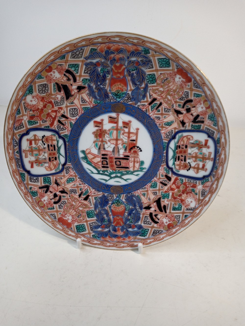 A four-piece Japanese Imari porcelain set featuring three patterned display plates and a matching small bowl decorated with European ship motifs in red, blue, and gold. View VII