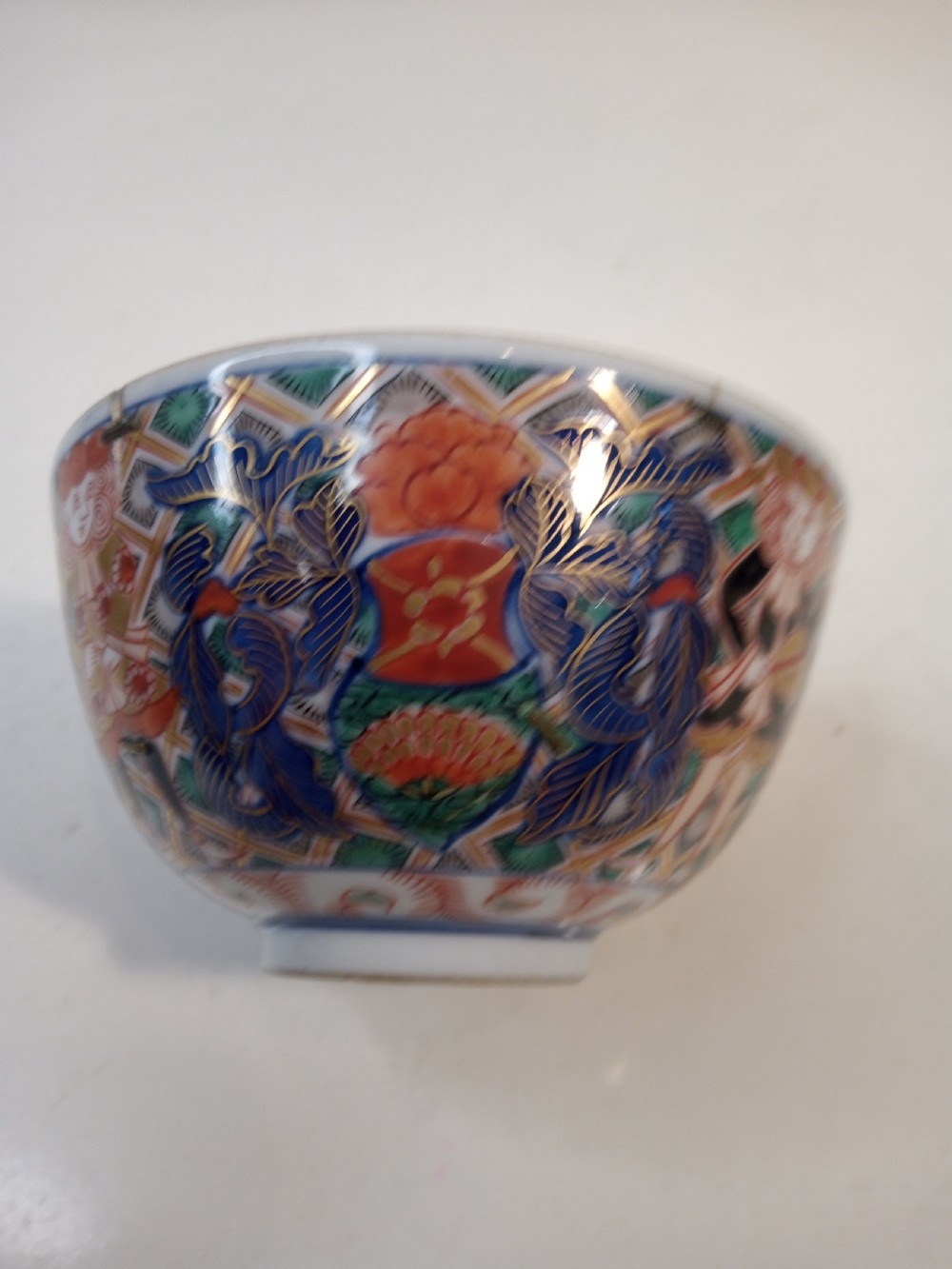A four-piece Japanese Imari porcelain set featuring three patterned display plates and a matching small bowl decorated with European ship motifs in red, blue, and gold. View X