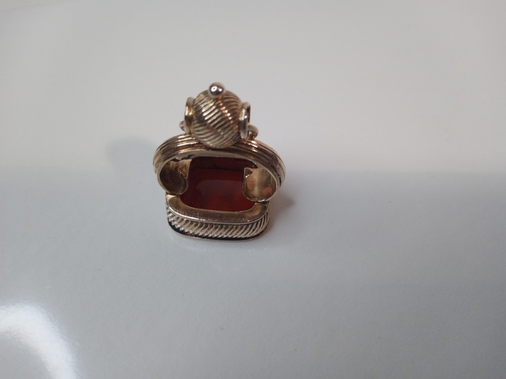 A 9 carat yellow gold watch fob seal featuring a textured gadrooned handle set with a rectangular reddish-brown carnelian stone base.