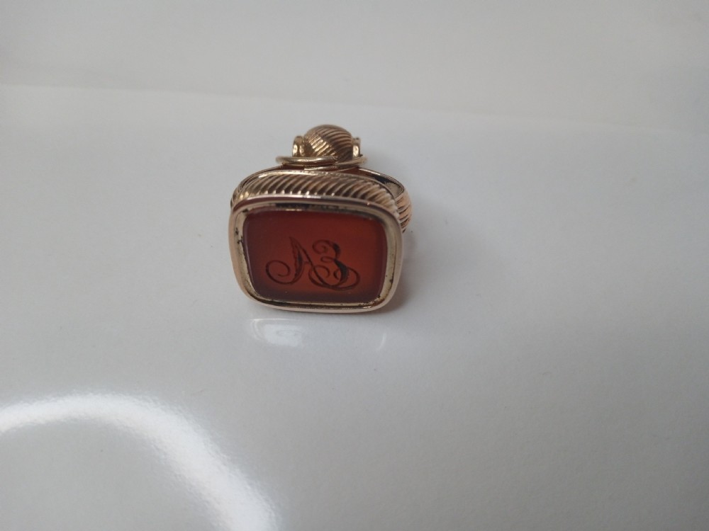 A 9 carat yellow gold watch fob seal featuring a textured gadrooned handle set with a rectangular reddish-brown carnelian stone base. View IV