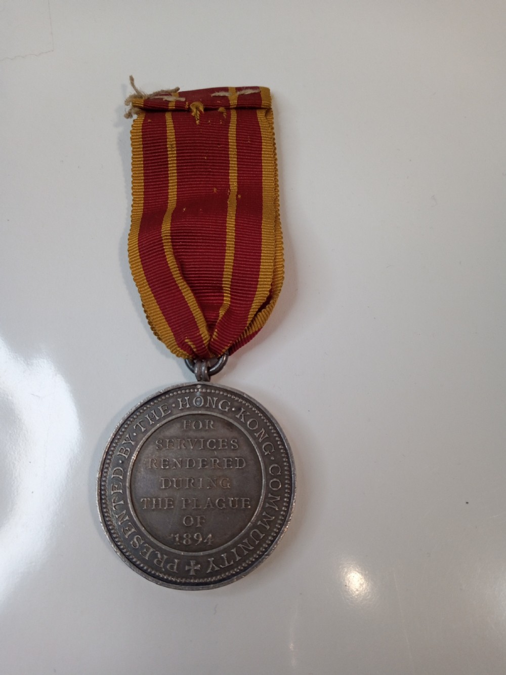 An antique silver circular service medal dated 1894 featuring relief figures and Chinese characters, suspended from a red and yellow striped silk ribbon. View III