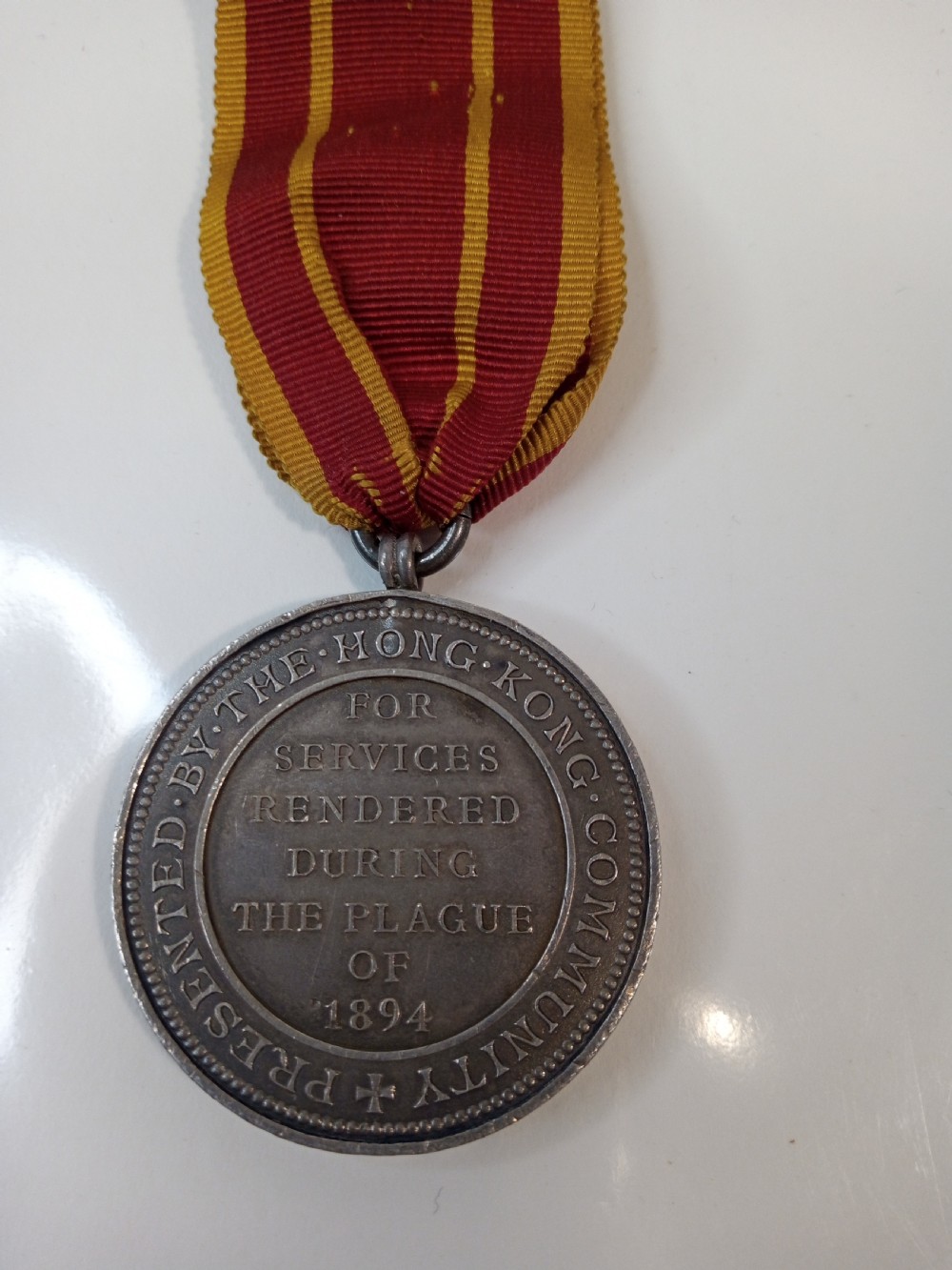 An antique silver circular service medal dated 1894 featuring relief figures and Chinese characters, suspended from a red and yellow striped silk ribbon. View IV