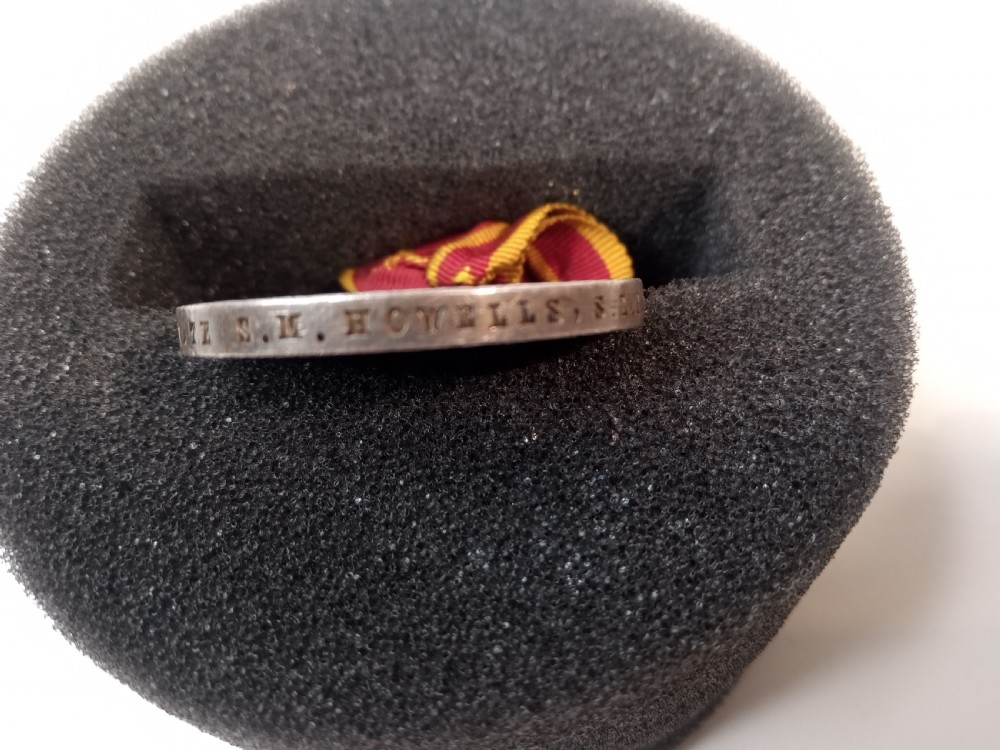 An antique silver circular service medal dated 1894 featuring relief figures and Chinese characters, suspended from a red and yellow striped silk ribbon. View V