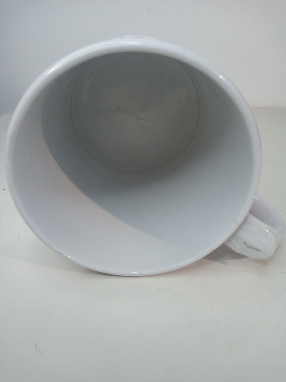 A cylindrical pink porcelain tankard featuring white moulded relief figures and a scrolled handle against a plain background. View VI