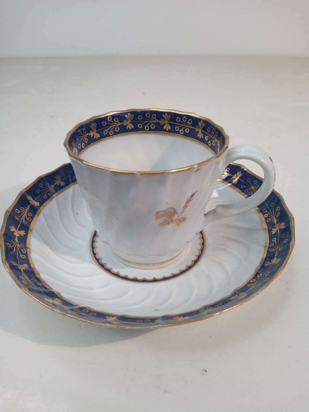 A Georgian Worcester spiral-fluted porcelain teacup and saucer with cobalt blue and gilt foliate borders. View II