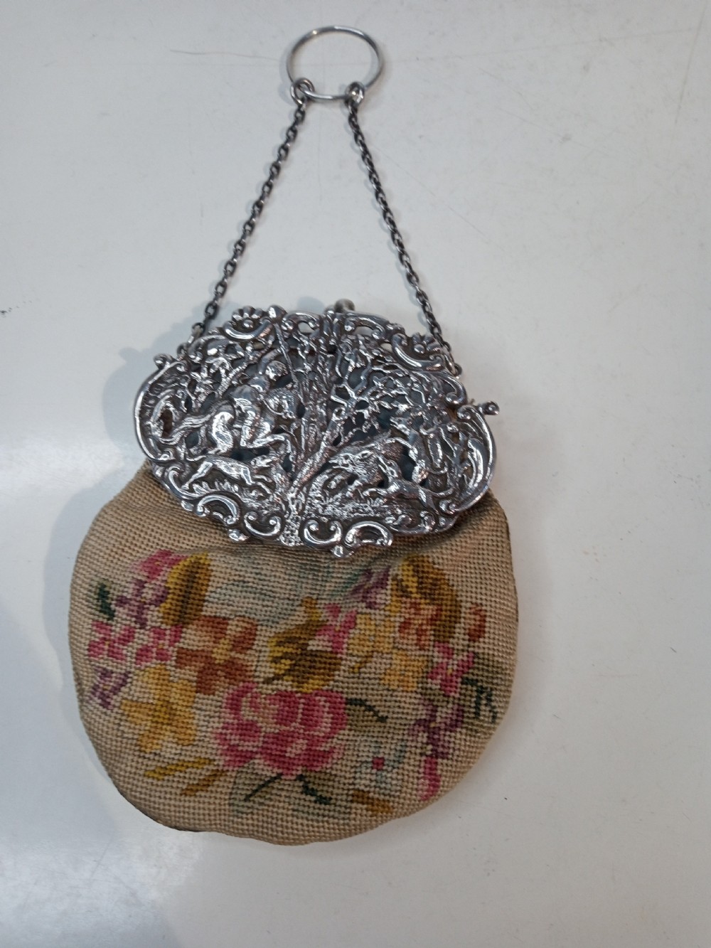 Late Victorian sterling silver evening purse featuring a pierced silver frame with a chain handle and a beige petit point needlepoint pouch with pink and yellow floral embroidery.
