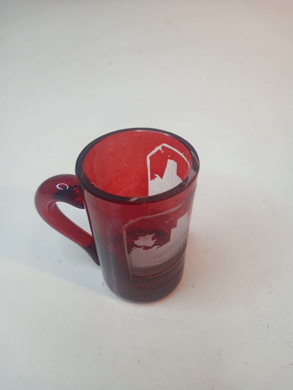 A late Victorian miniature ruby glass tankard with an applied red handle and a white etched architectural motif on the body. View II