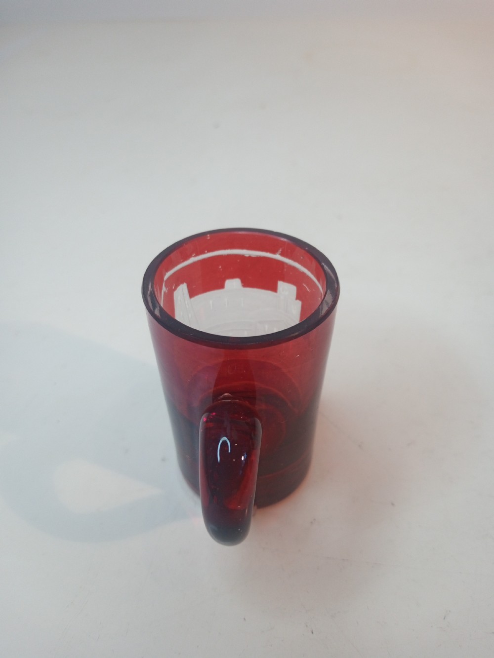 A late Victorian miniature ruby glass tankard with an applied red handle and a white etched architectural motif on the body. View IV
