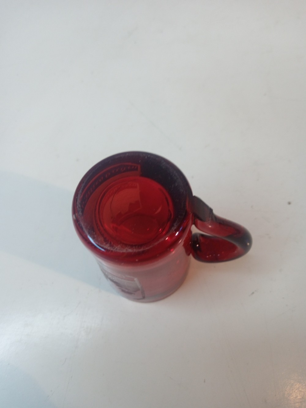 A late Victorian miniature ruby glass tankard with an applied red handle and a white etched architectural motif on the body. View V