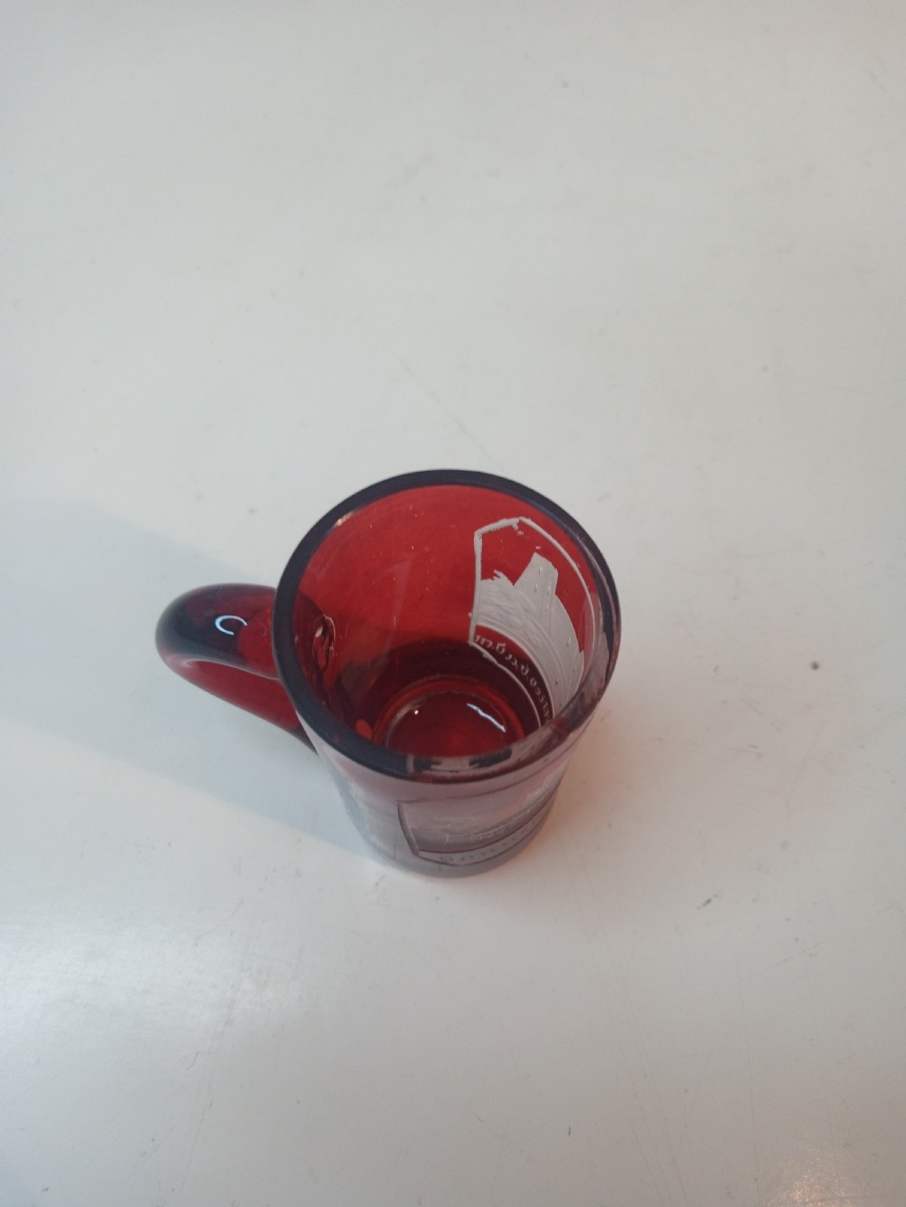 A late Victorian miniature ruby glass tankard with an applied red handle and a white etched architectural motif on the body. View VI