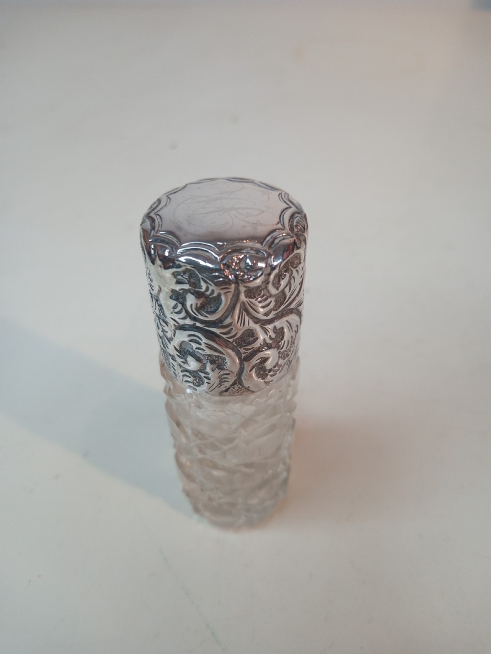 A cylindrical Victorian cut glass scent bottle topped with a heavily chased silver cap featuring floral motifs. View II