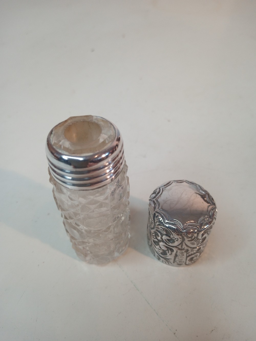 A cylindrical Victorian cut glass scent bottle topped with a heavily chased silver cap featuring floral motifs. View III