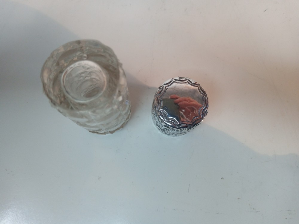 A cylindrical Victorian cut glass scent bottle topped with a heavily chased silver cap featuring floral motifs. View V