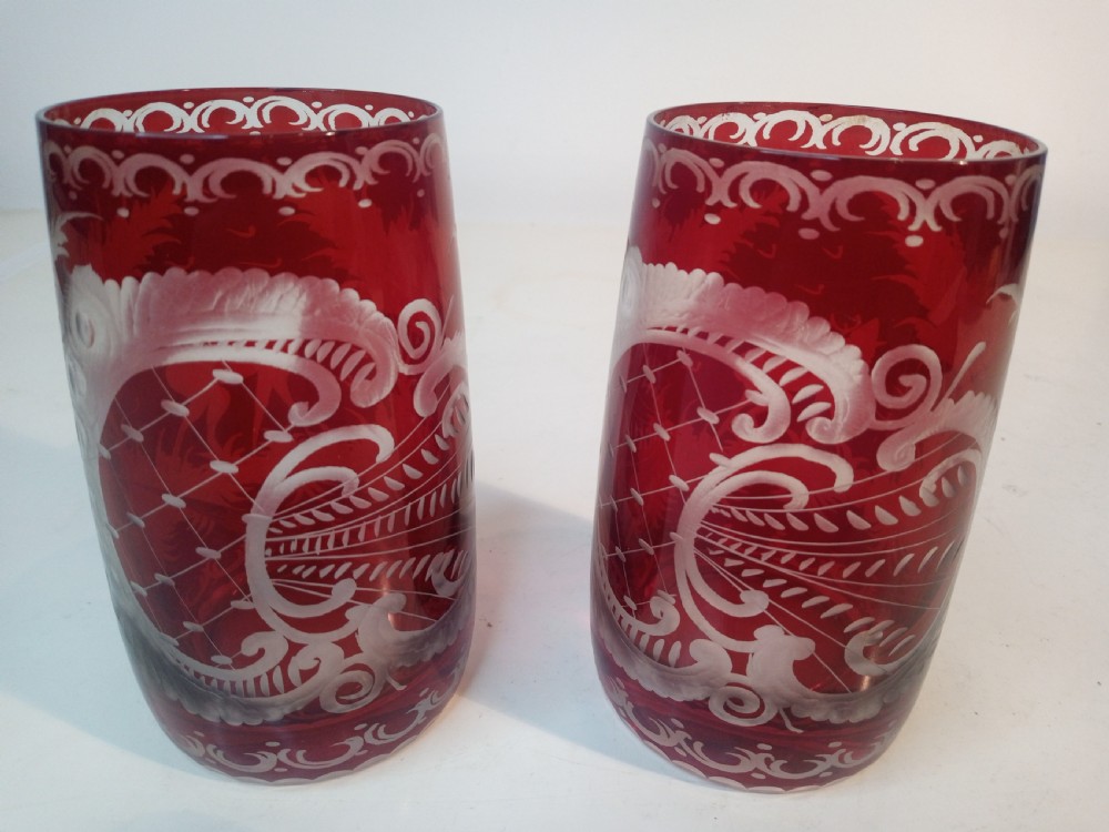 A pair of ruby red glass tumblers featuring white wheel-engraved stag and forest motifs with decorative scrollwork borders. View II