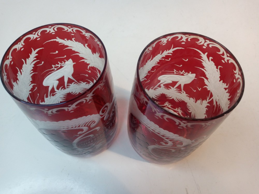 A pair of ruby red glass tumblers featuring white wheel-engraved stag and forest motifs with decorative scrollwork borders. View III