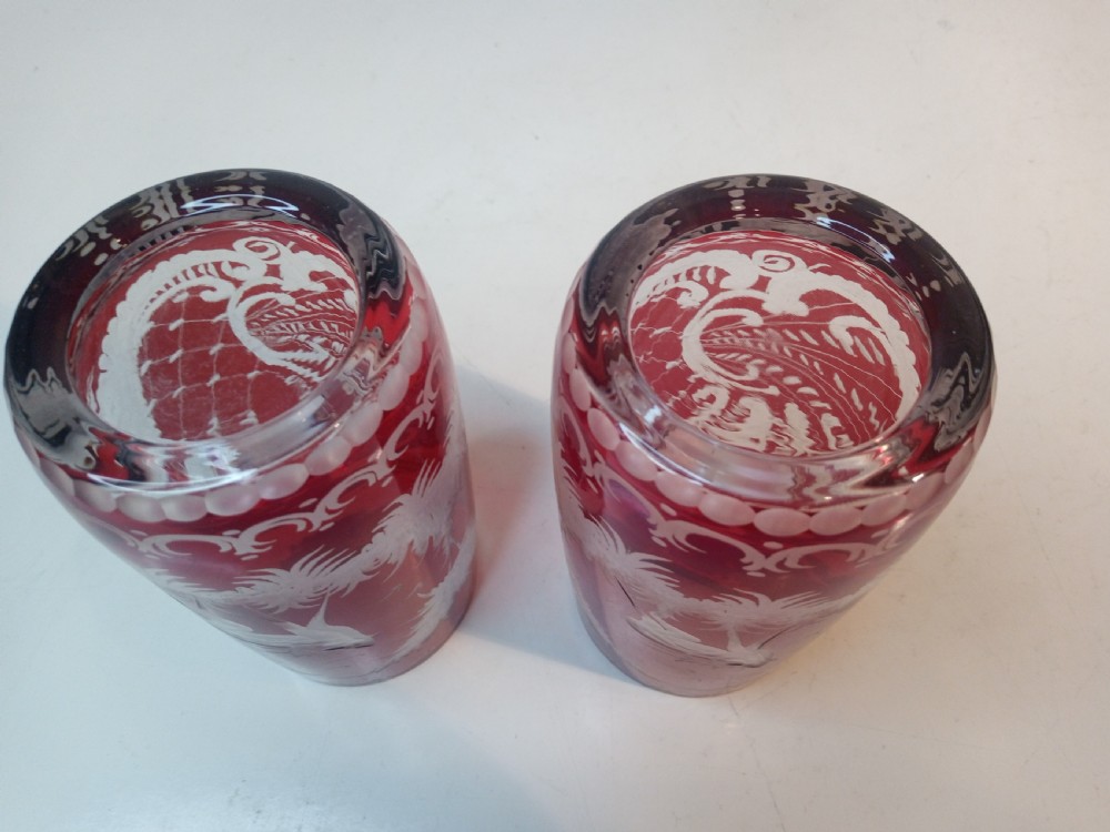 A pair of ruby red glass tumblers featuring white wheel-engraved stag and forest motifs with decorative scrollwork borders. View IV