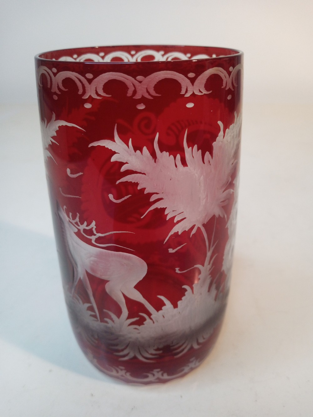 A pair of ruby red glass tumblers featuring white wheel-engraved stag and forest motifs with decorative scrollwork borders. View V