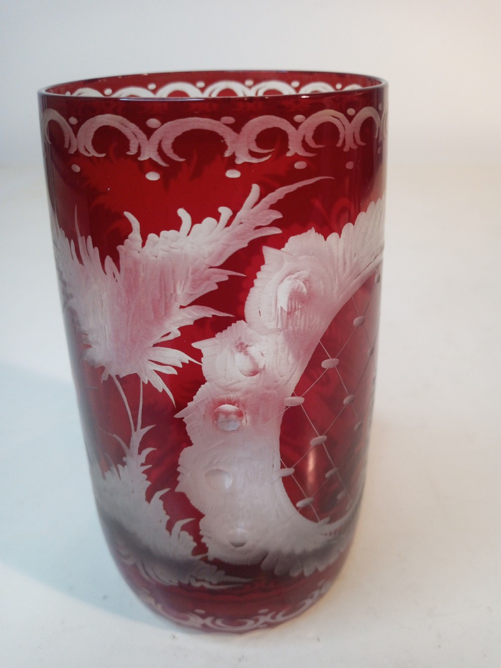 A pair of ruby red glass tumblers featuring white wheel-engraved stag and forest motifs with decorative scrollwork borders. View VI