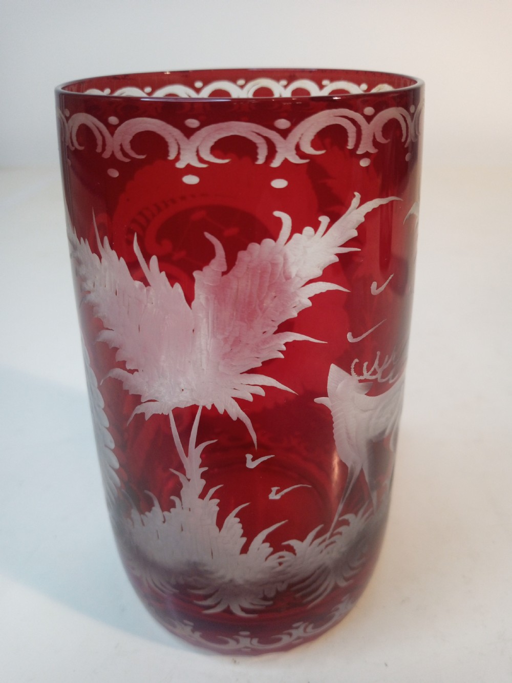 A pair of ruby red glass tumblers featuring white wheel-engraved stag and forest motifs with decorative scrollwork borders. View IX