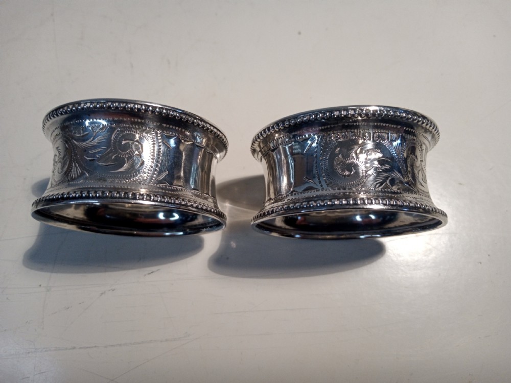 A pair of engraved sterling silver napkin rings with beaded rims and hallmarked details resting on a light surface.