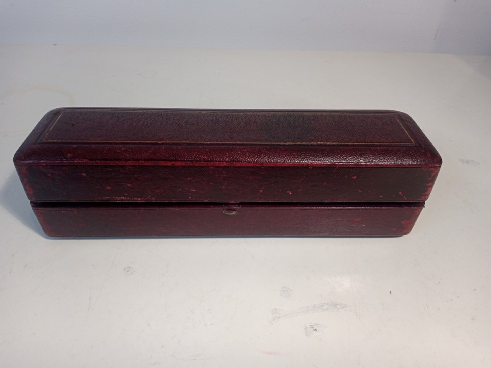 A set of six silver-plated napkin rings with beaded rims displayed inside a dark red fitted presentation case lined with blue velvet. View II