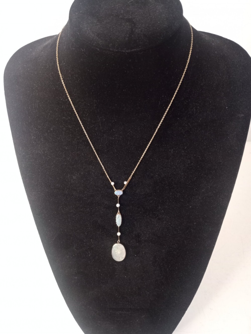 An Art Deco period gold chain necklace featuring a vertical drop pendant set with cabochon opals and small pearls.