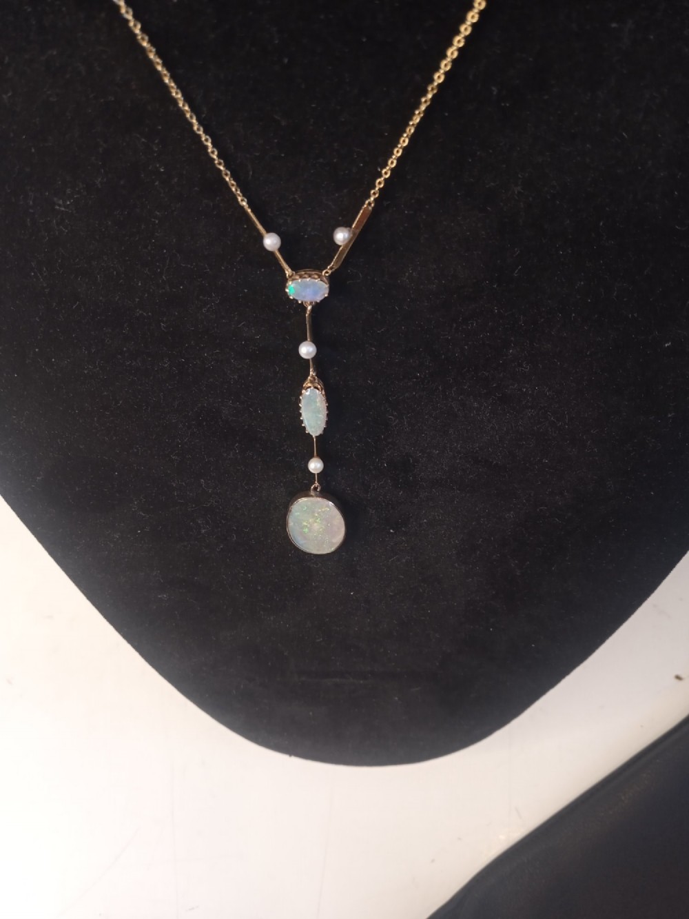 An Art Deco period gold chain necklace featuring a vertical drop pendant set with cabochon opals and small pearls. View V