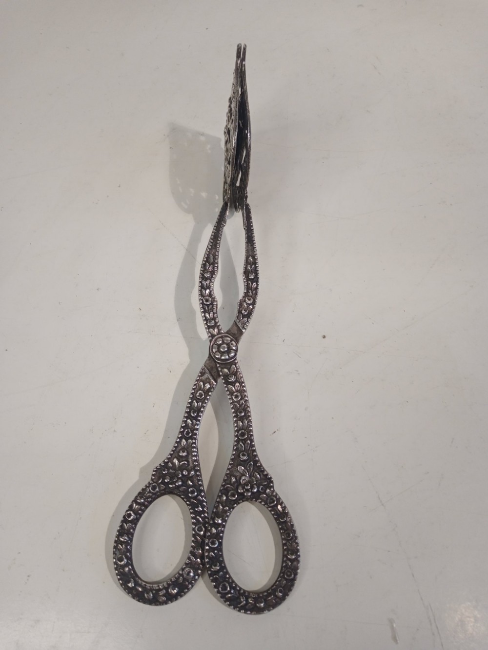 A pair of antique German silver scissor-style cake tongs featuring pierced relief blades and textured arms. View II