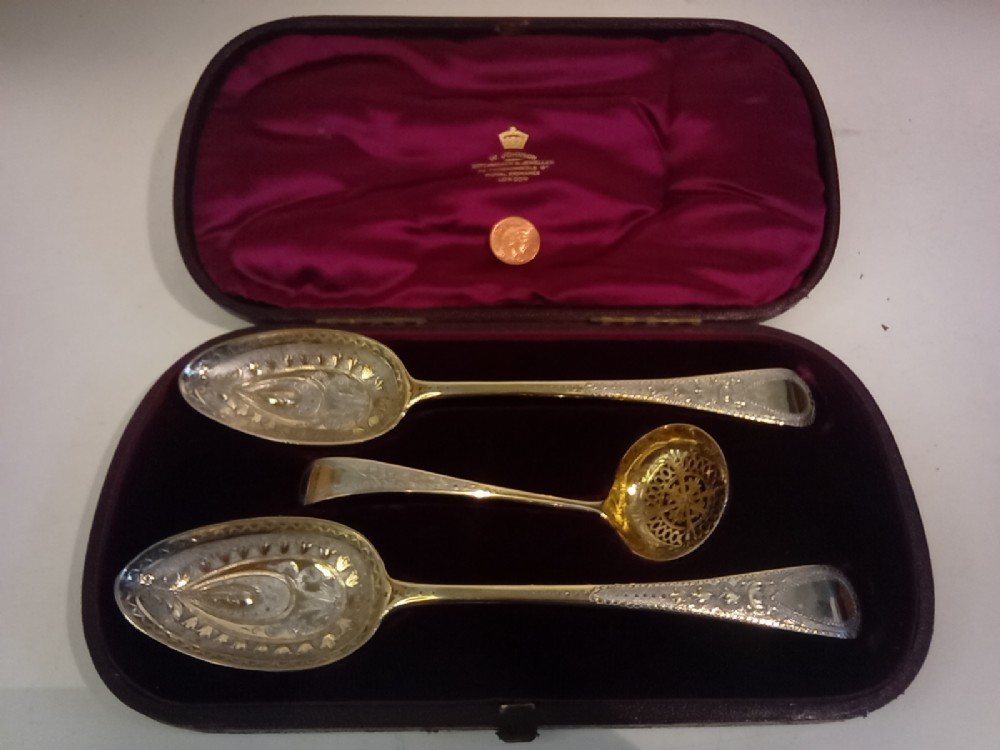 A dark presentation case lined with purple silk containing two embossed silver-gilt berry spoons and a pierced sugar sifter spoon. View II