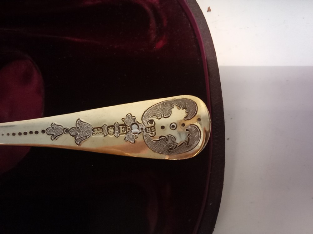 A dark presentation case lined with purple silk containing two embossed silver-gilt berry spoons and a pierced sugar sifter spoon. View V