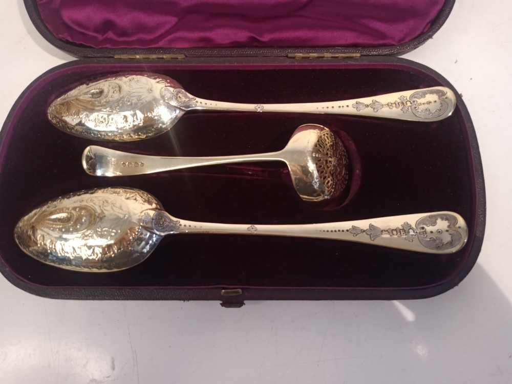 A dark presentation case lined with purple silk containing two embossed silver-gilt berry spoons and a pierced sugar sifter spoon. View VI