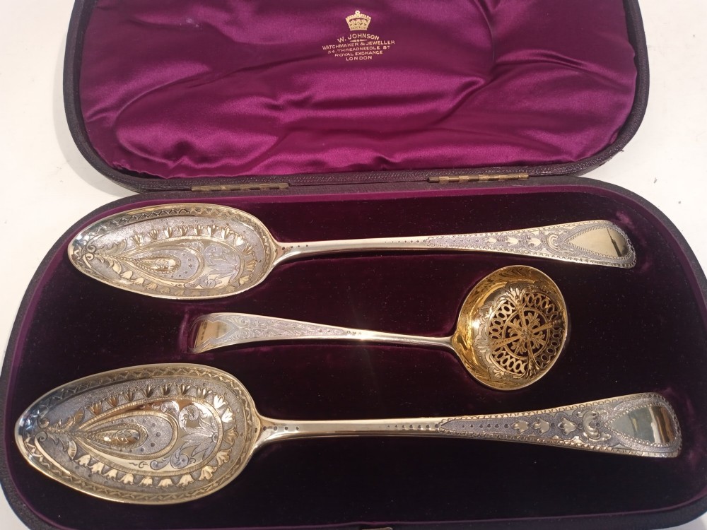 A dark presentation case lined with purple silk containing two embossed silver-gilt berry spoons and a pierced sugar sifter spoon. View VII