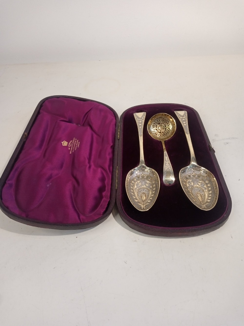 A dark presentation case lined with purple silk containing two embossed silver-gilt berry spoons and a pierced sugar sifter spoon. View IX
