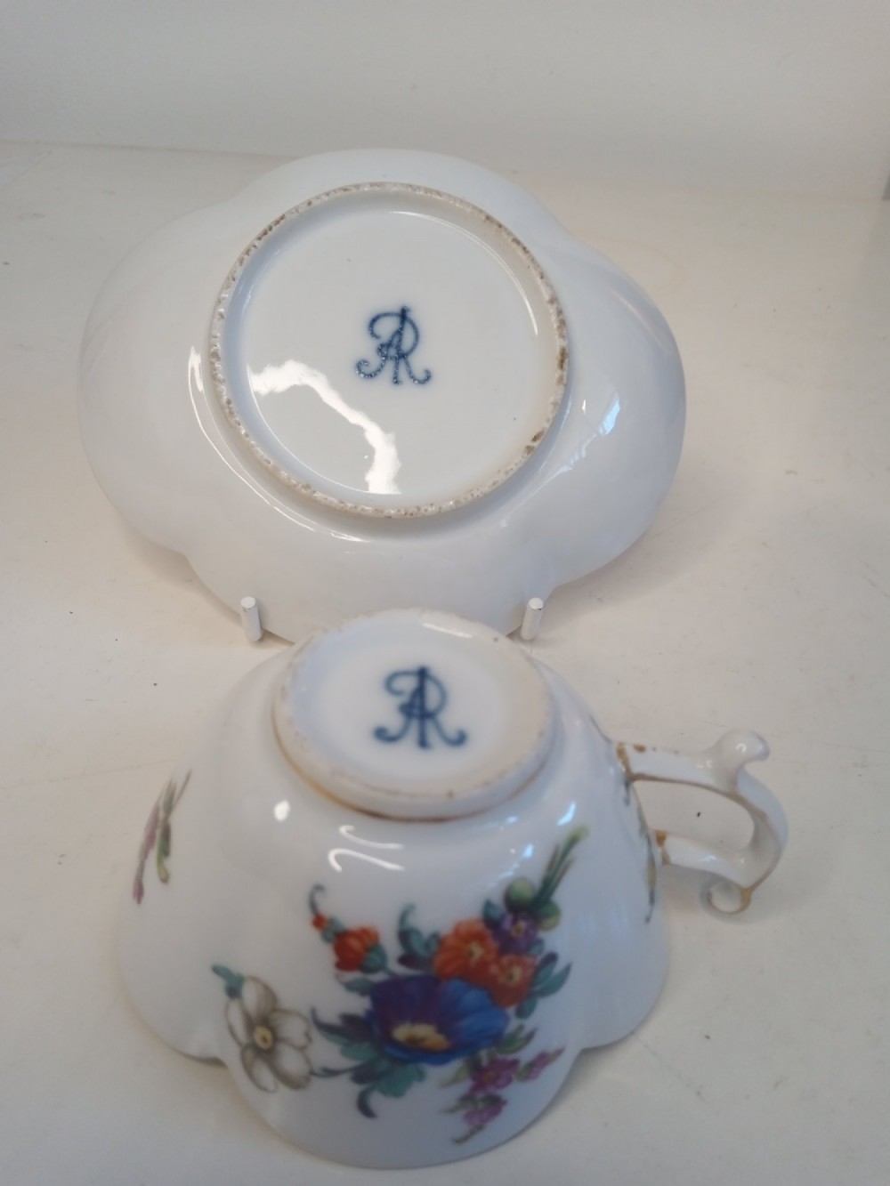A white porcelain teacup and scalloped saucer decorated with hand-painted multicoloured floral sprays and gold gilded rims. View V