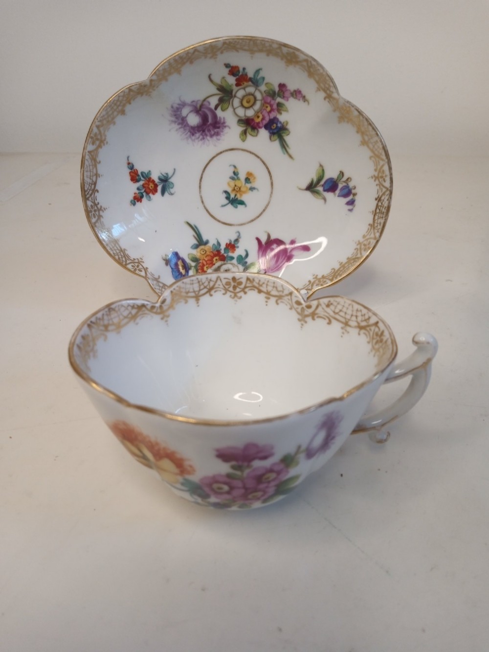 A white porcelain teacup and scalloped saucer decorated with hand-painted multicoloured floral sprays and gold gilded rims. View VI