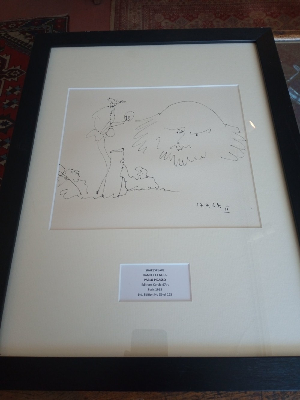 A framed black line drawing print by Pablo Picasso featuring minimalist figures on off-white paper within a black wooden frame.