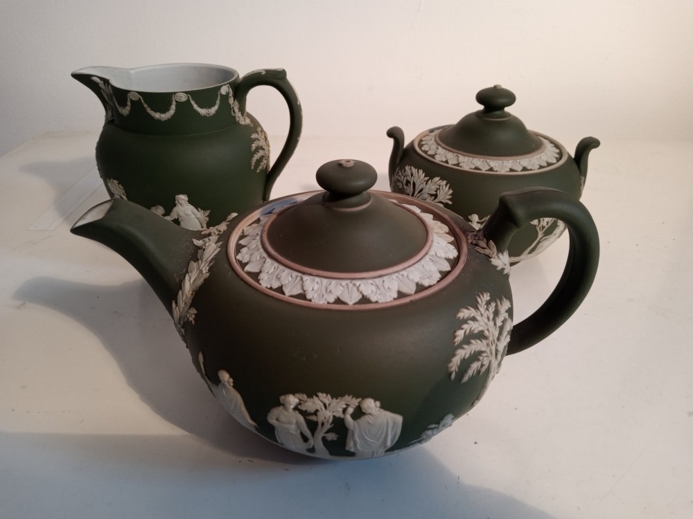 A late nineteenth-century three-piece olive green Wedgwood jasperware bachelor tea set adorned with white Neoclassical relief figures and foliage.