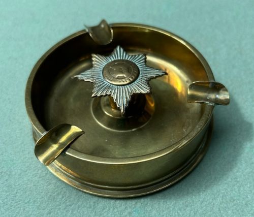 fig 4. Circular brass trench art ashtray formed from a shell casing with three cigarette rests and a central star-shaped military emblem.