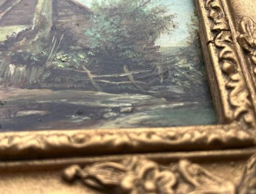 An antique oil painting on panel depicting a rural British cottage surrounded by trees, set within an ornate gilt frame. View X
