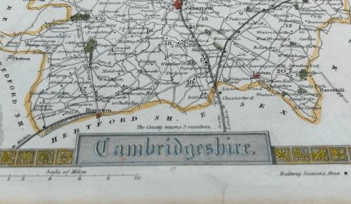 fig 1. A hand-coloured 19th-century engraved map of Cambridgeshire by Thomas Moule framed by Gothic architectural borders, heraldic shields, and vignettes of Ely Cathedral and Wimpole Hall.