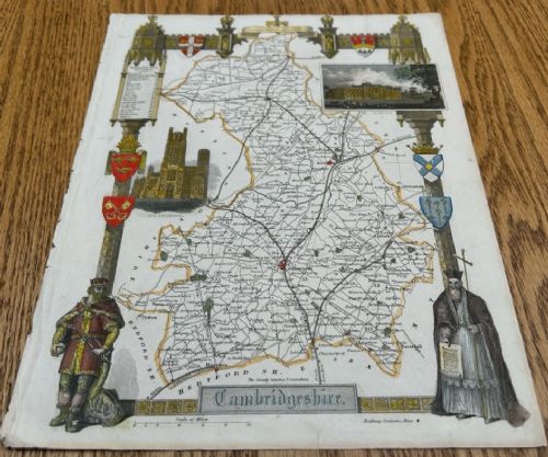 A hand-coloured 19th-century engraved map of Cambridgeshire by Thomas Moule framed by Gothic architectural borders, heraldic shields, and vignettes of Ely Cathedral and Wimpole Hall. View III