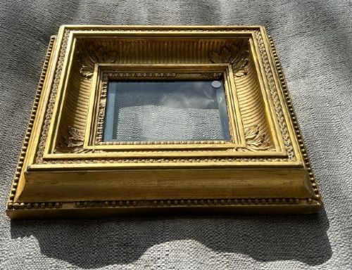 A square, deep-profile antique giltwood picture frame featuring fluted channel moulding and carved acanthus leaf corner ornaments. View V
