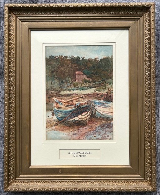 An antique watercolour painting depicting wooden boats along the River Esk near Whitby, presented in a gold gilt frame with a white mount.
