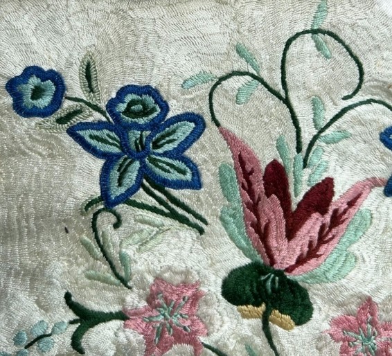 An early 20th-century framed floral embroidery panel featuring colourful hand-stitched blossoms on a cream background set within an ornate relief frame. View III