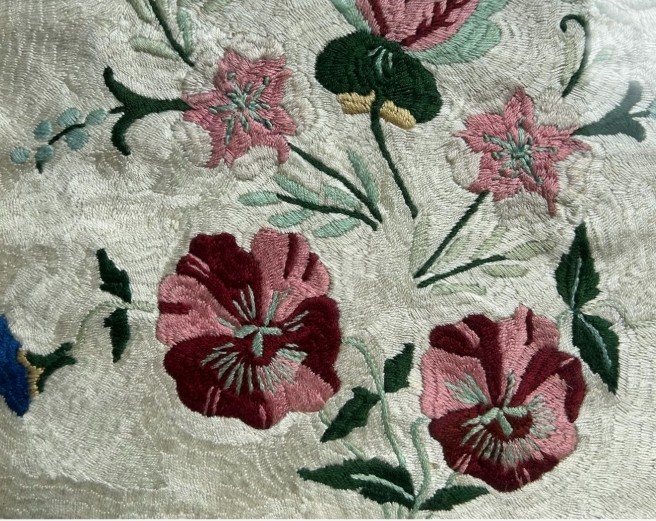 An early 20th-century framed floral embroidery panel featuring colourful hand-stitched blossoms on a cream background set within an ornate relief frame. View V
