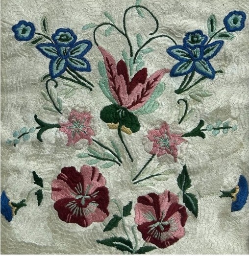 An early 20th-century framed floral embroidery panel featuring colourful hand-stitched blossoms on a cream background set within an ornate relief frame. View VII